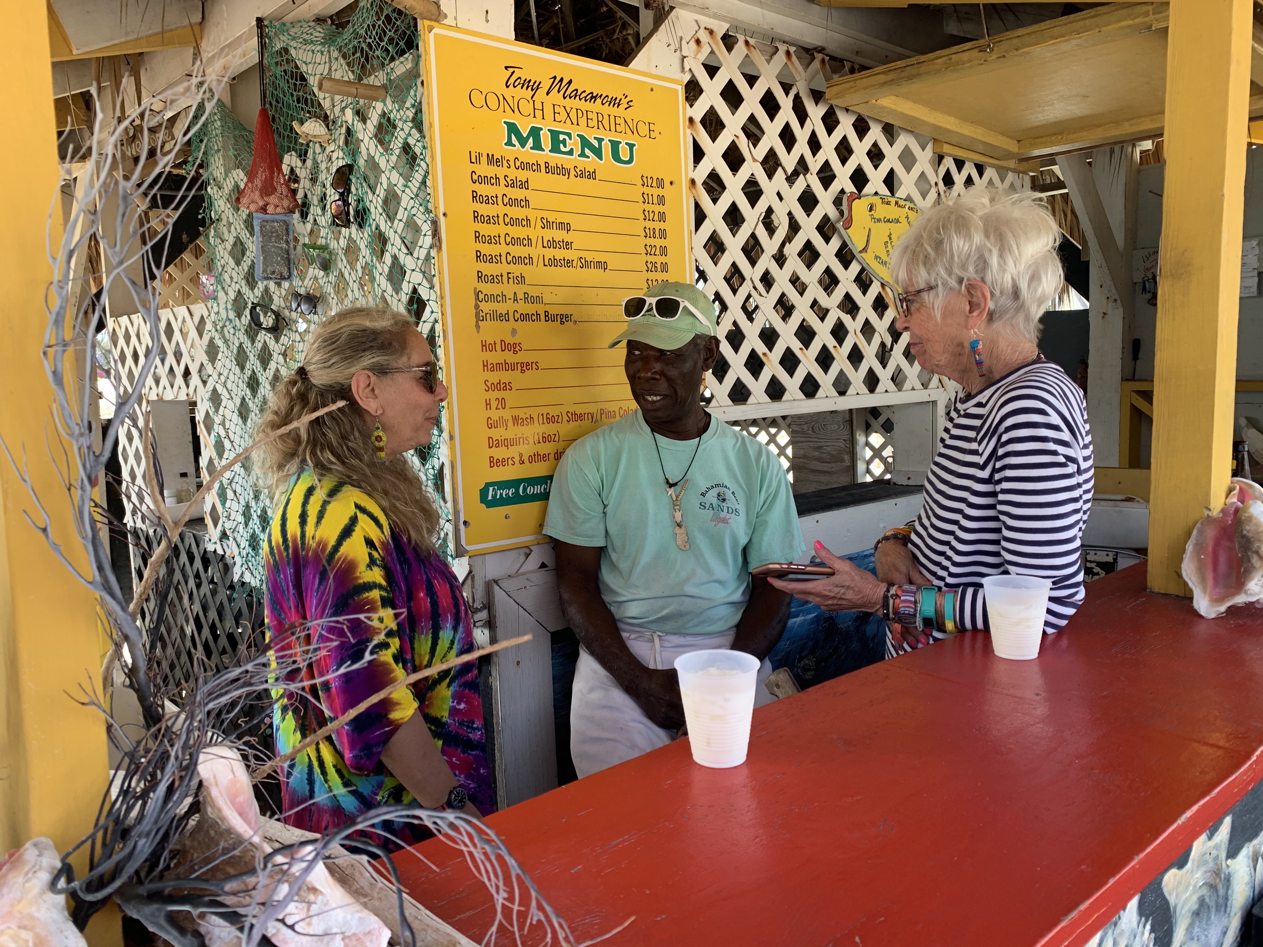 Caribbean travel writers Melanie Reffes (L) and Gay Nagle Myers (R) visit Anthony Hanna, proprietor of Tony Macaroni’s Conch Experience, for lunch during a familiarization tour of Grand Bahama.